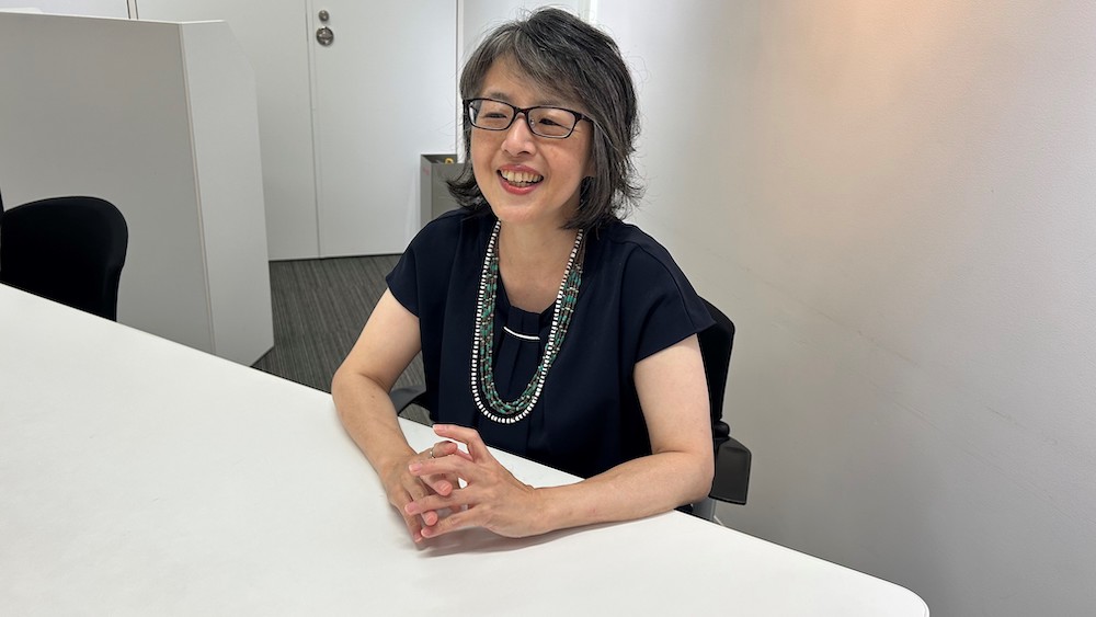 着席し、インタビューに笑顔で答える女性